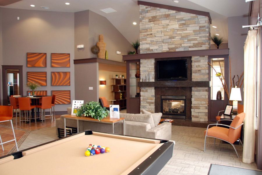 Modern lounge with a pool table, fireplace, TV, seating area, and orange-themed decor accents.