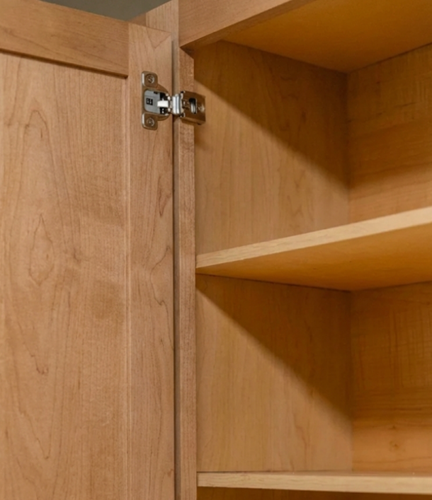 Close-up of an open wooden cabinet showing door hinge and empty shelves inside.