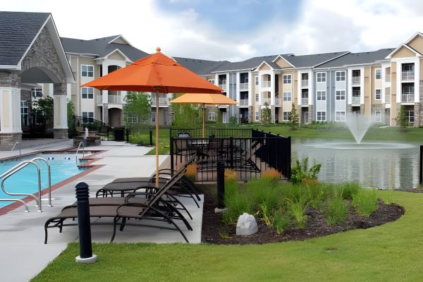 Apartment poolside with lounge chairs, orange umbrella, and a pond with a fountain in the background.