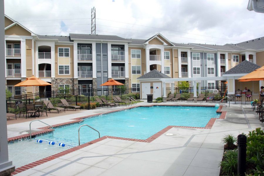 Outdoor swimming pool with lounge chairs, umbrellas, and a three-story apartment building in the background.
