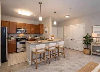 Modern kitchen with stainless steel appliances, island with three chairs, and neutral decor.