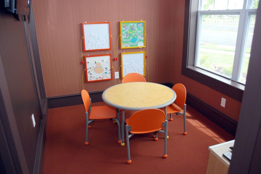 A small playroom with a round table, four orange chairs, and wall-mounted activity boards.