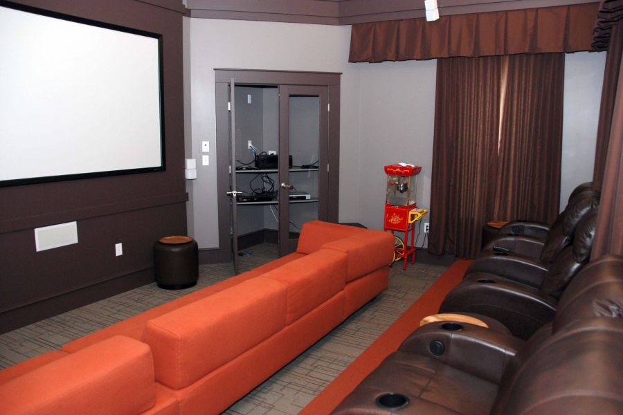 Home theater room with a projector screen, leather seats, an orange couch, and a popcorn machine.