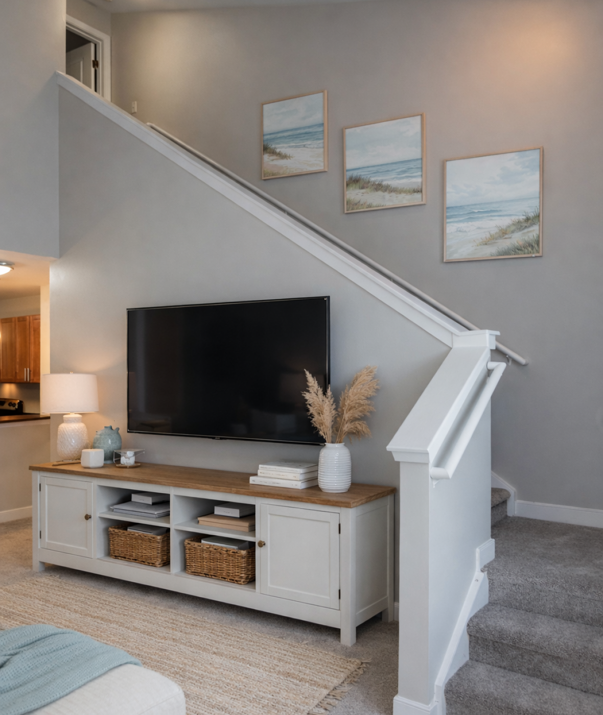 Modern living room with TV stand, wall art, baskets, and a staircase with gray walls and carpeting.